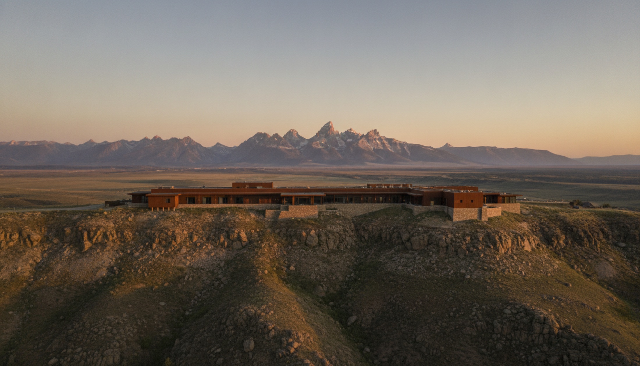 Amangani'nin East Gros Ventre Butte üzerindeki gün doğumu silüeti, arka planda Grand Teton sırası