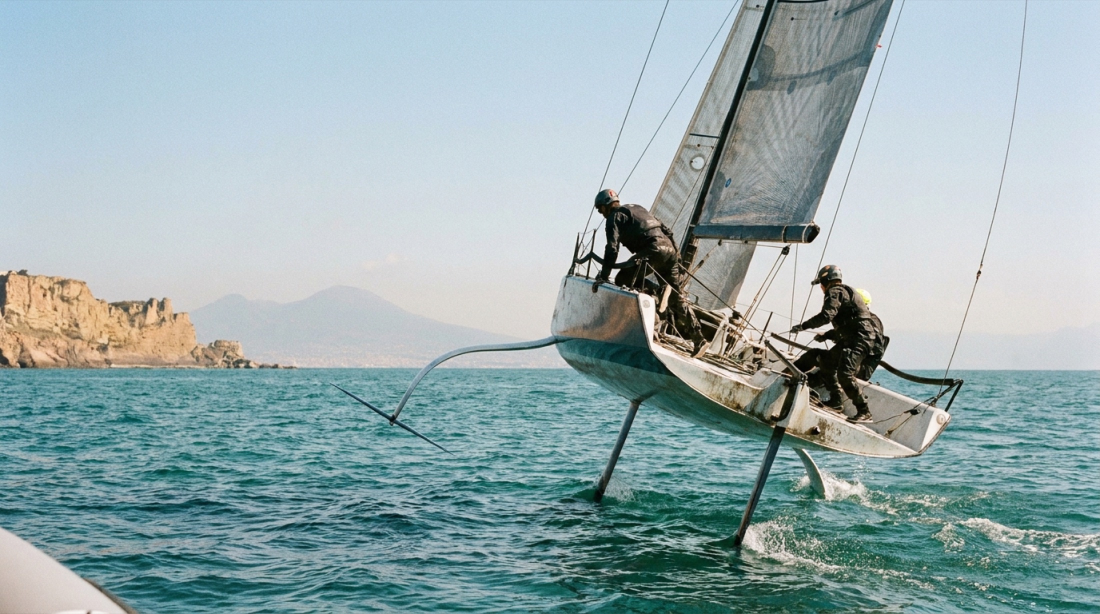 America's Cup foiling yarış teknesi Napoli körfezinde su üzerinde uçarken, arka planda Vezüv silueti