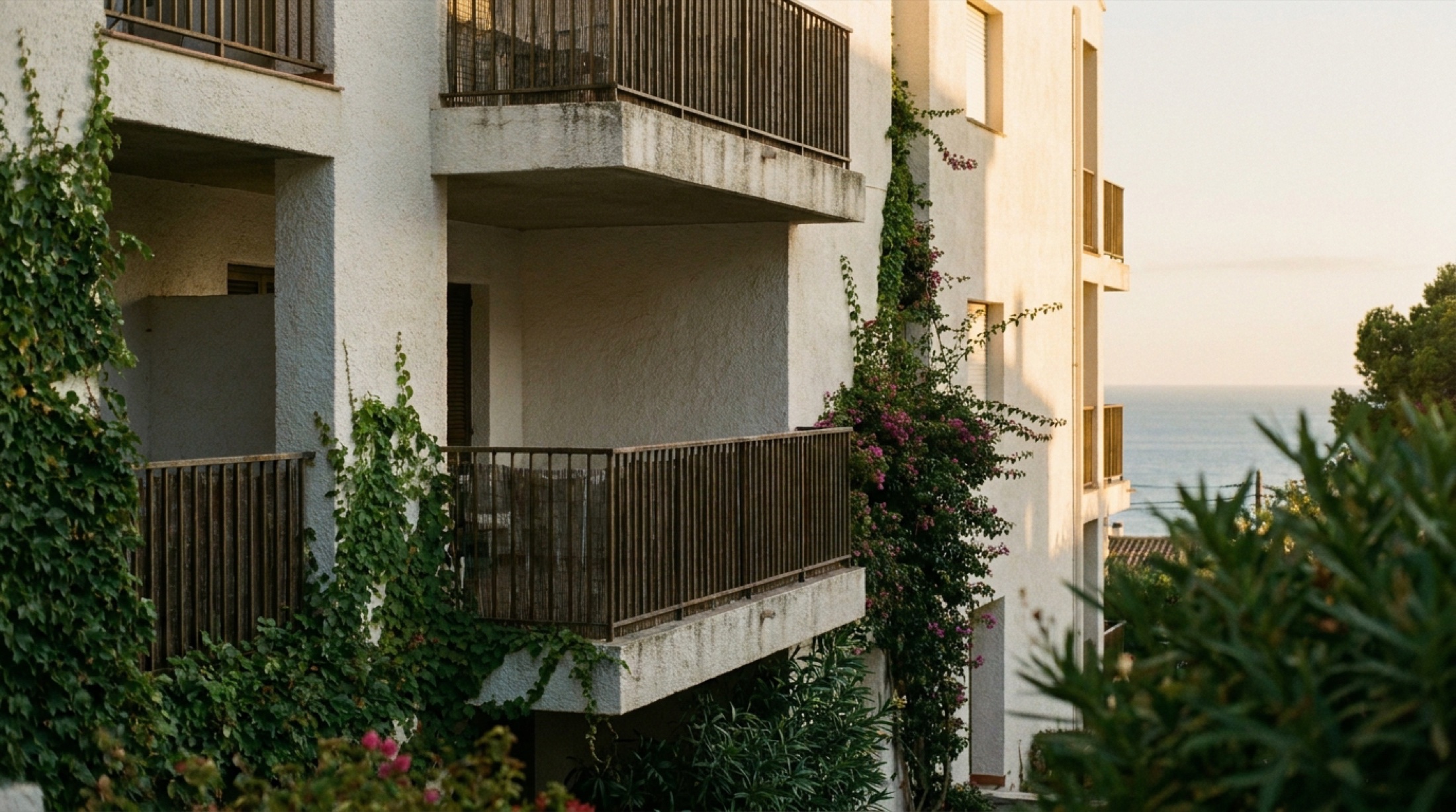 Akdeniz ışığında modern konut binası cephesi, balkonlar ve yeşil bitki örtüsü