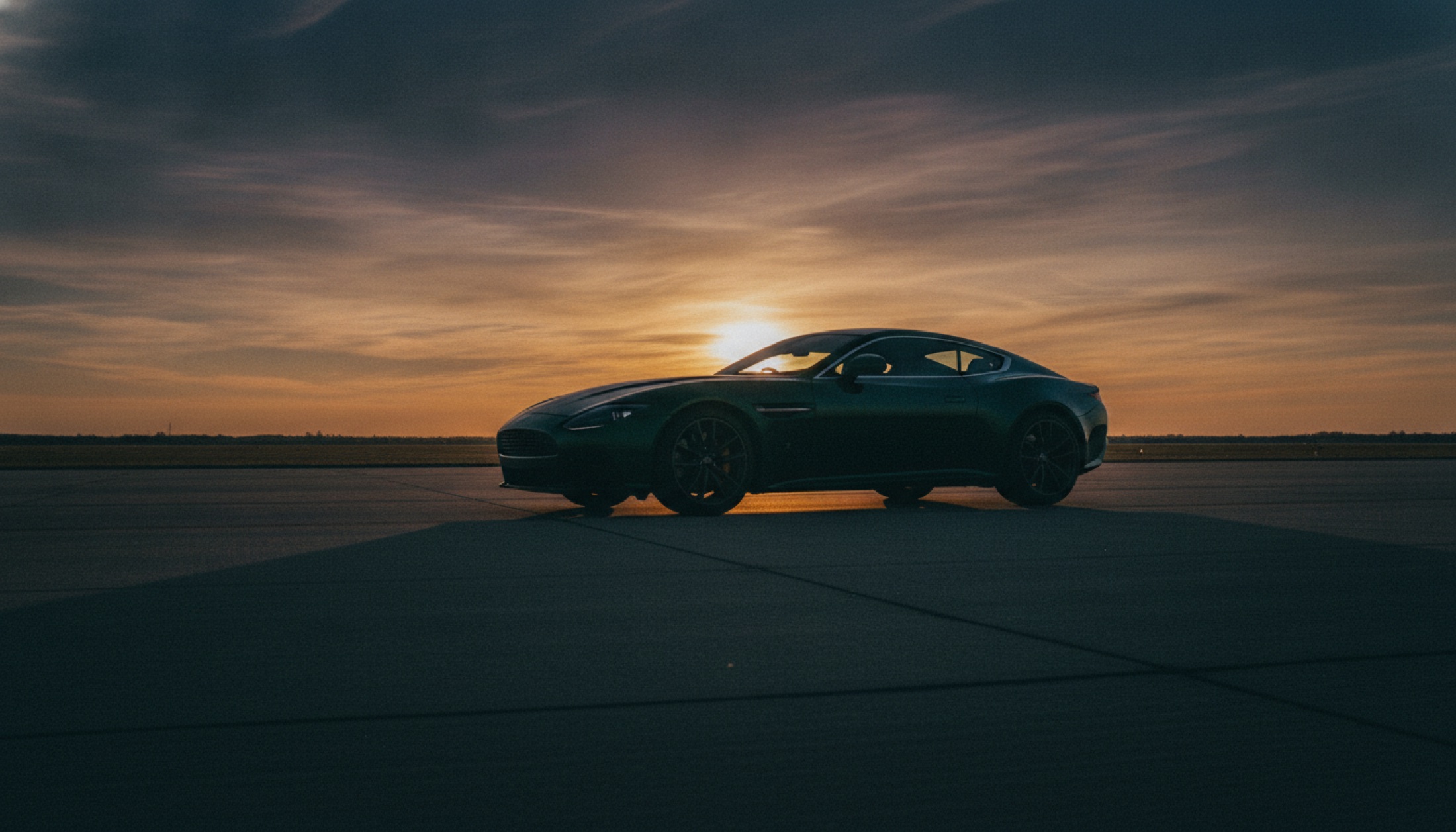 2026 Aston Martin Vanquish karbon fiber gövdesiyle alacakaranlıkta boş bir pist üzerinde, uzun gölgeler