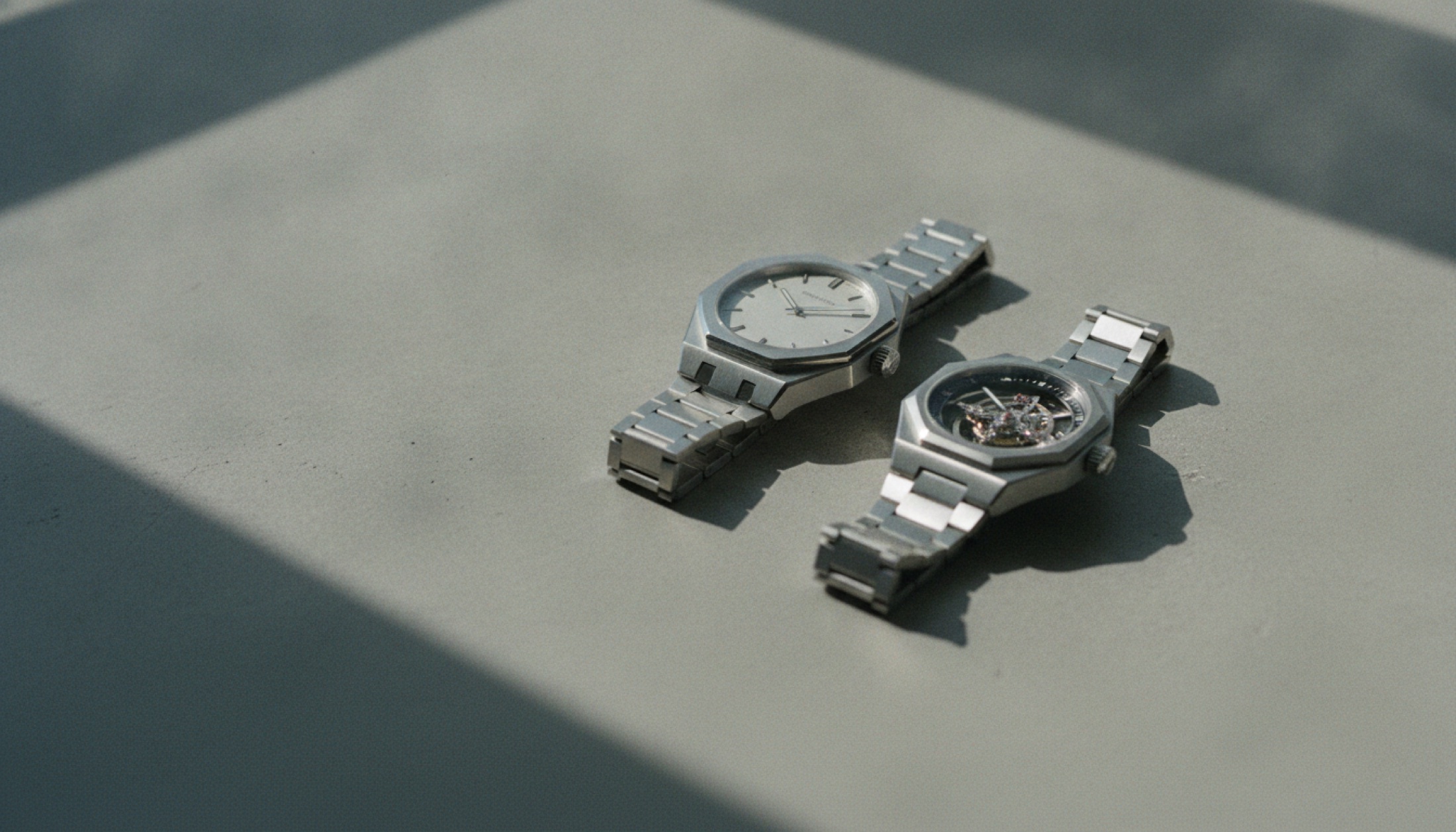 Czapek Antarctique Tourbillon ve Zenith Defy Revival A3643 saatleri beton yüzey üzerinde yan yana, doğal yan ışıkla