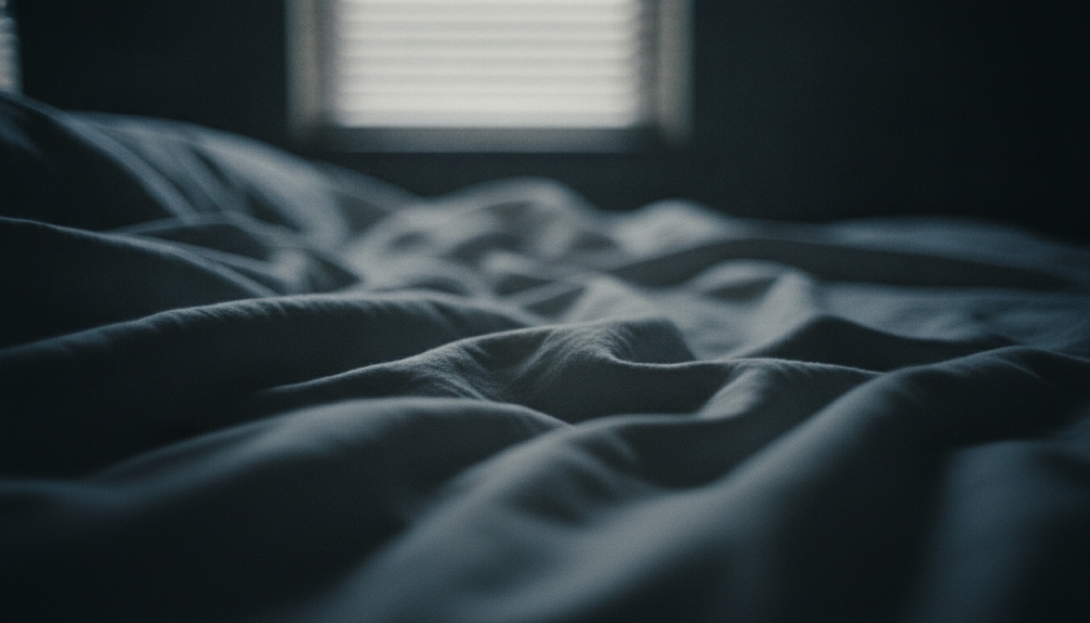 Gece ışığının kırık çizgiler halinde düştüğü karanlık bir yatak odası, linen dokusu detayı