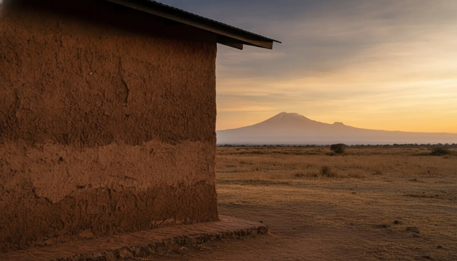Amboseli'de enkaji formundan türetilmiş toprak sıvalı Kitirua Plains Lodge süitinin cephesi, arka planda Kilimanjaro silueti
