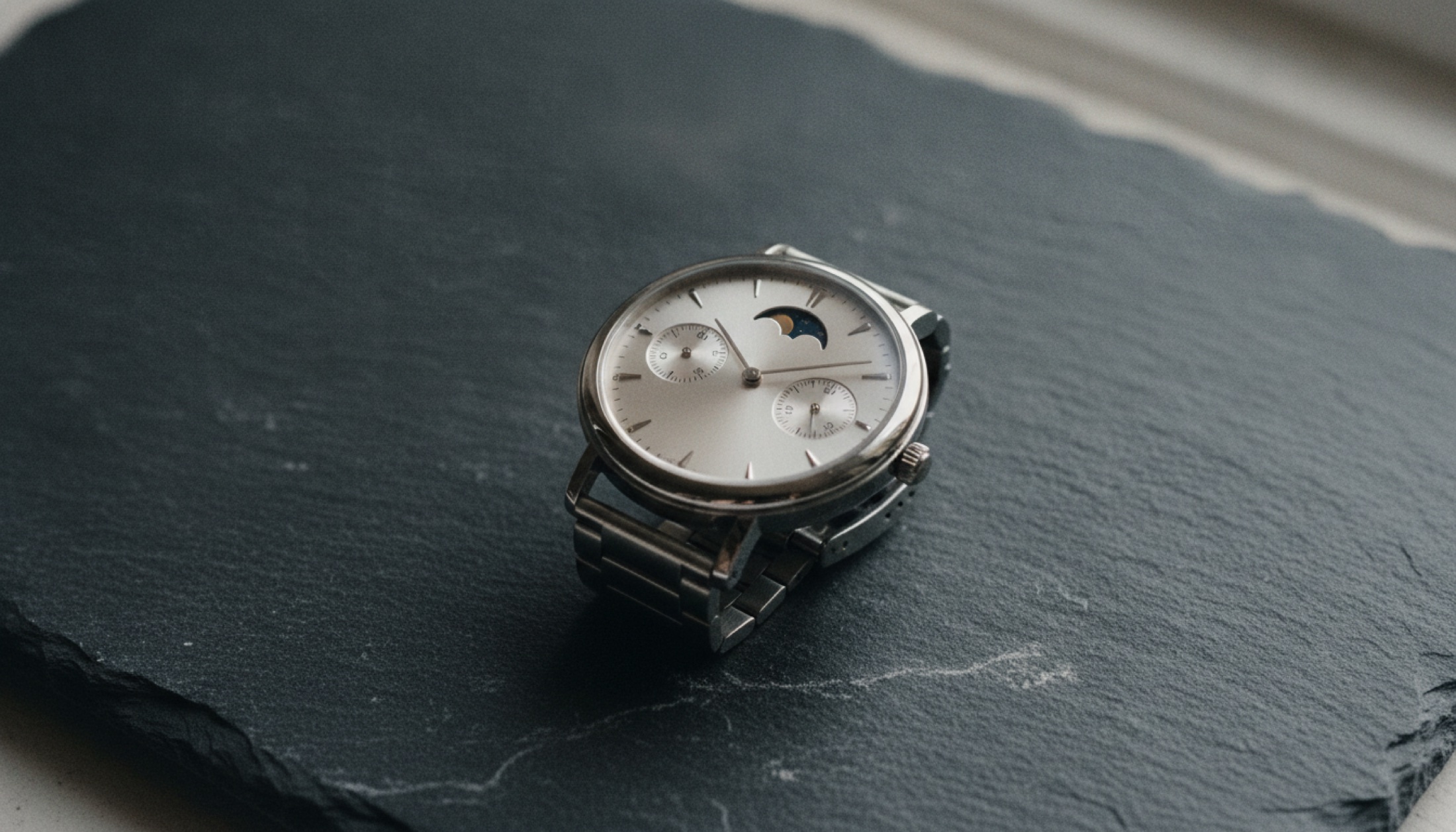 36mm gümüş kadranı ve ay evresi komplikasyonuyla küçük kol saati, arduvaz yüzey üzerinde üstten görünüm