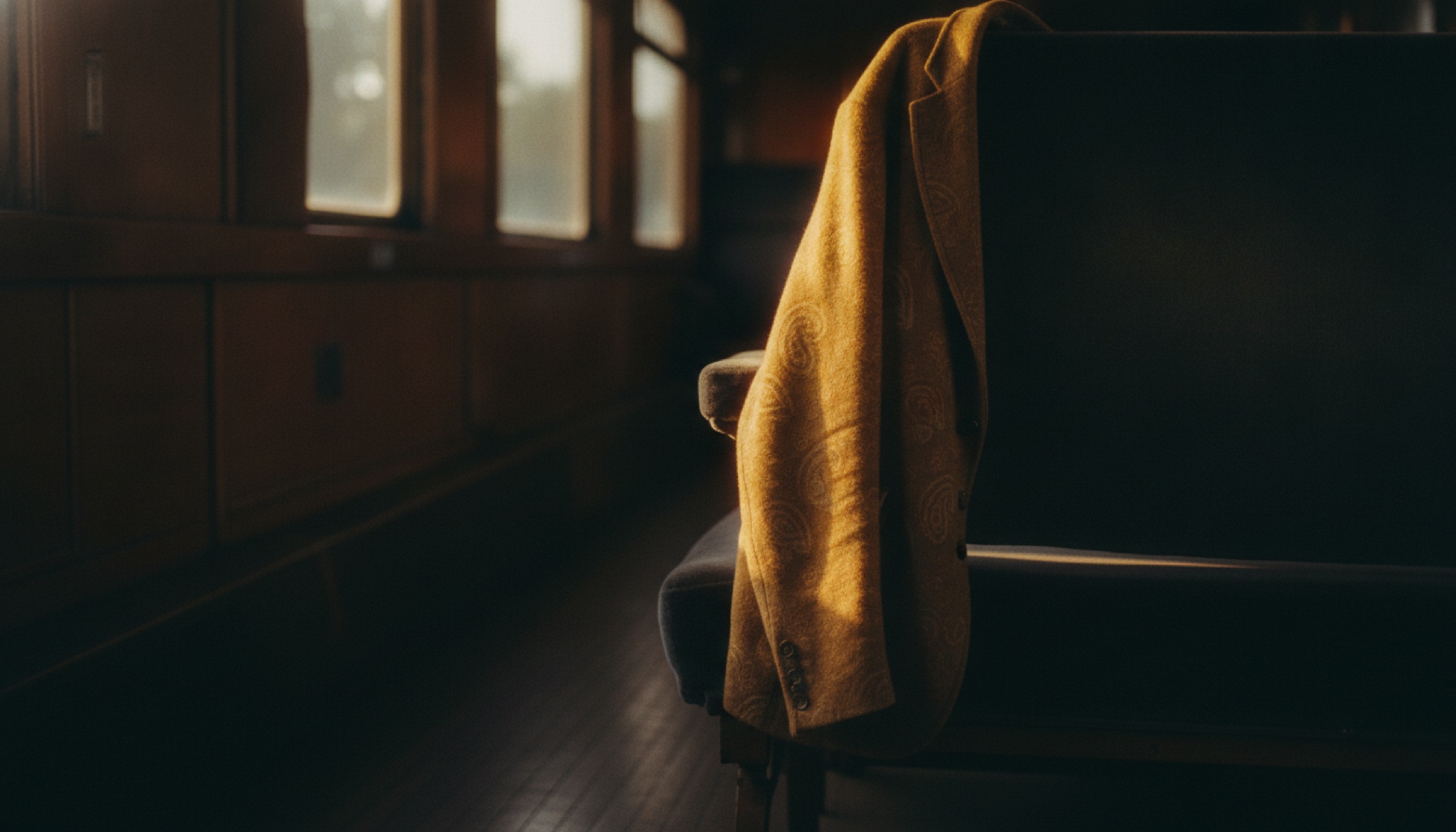 Paisley jakarli kaşmir ceket, tren kompartımanı koltuğunun sırtlığına asılı, pencereden giren amber ışık