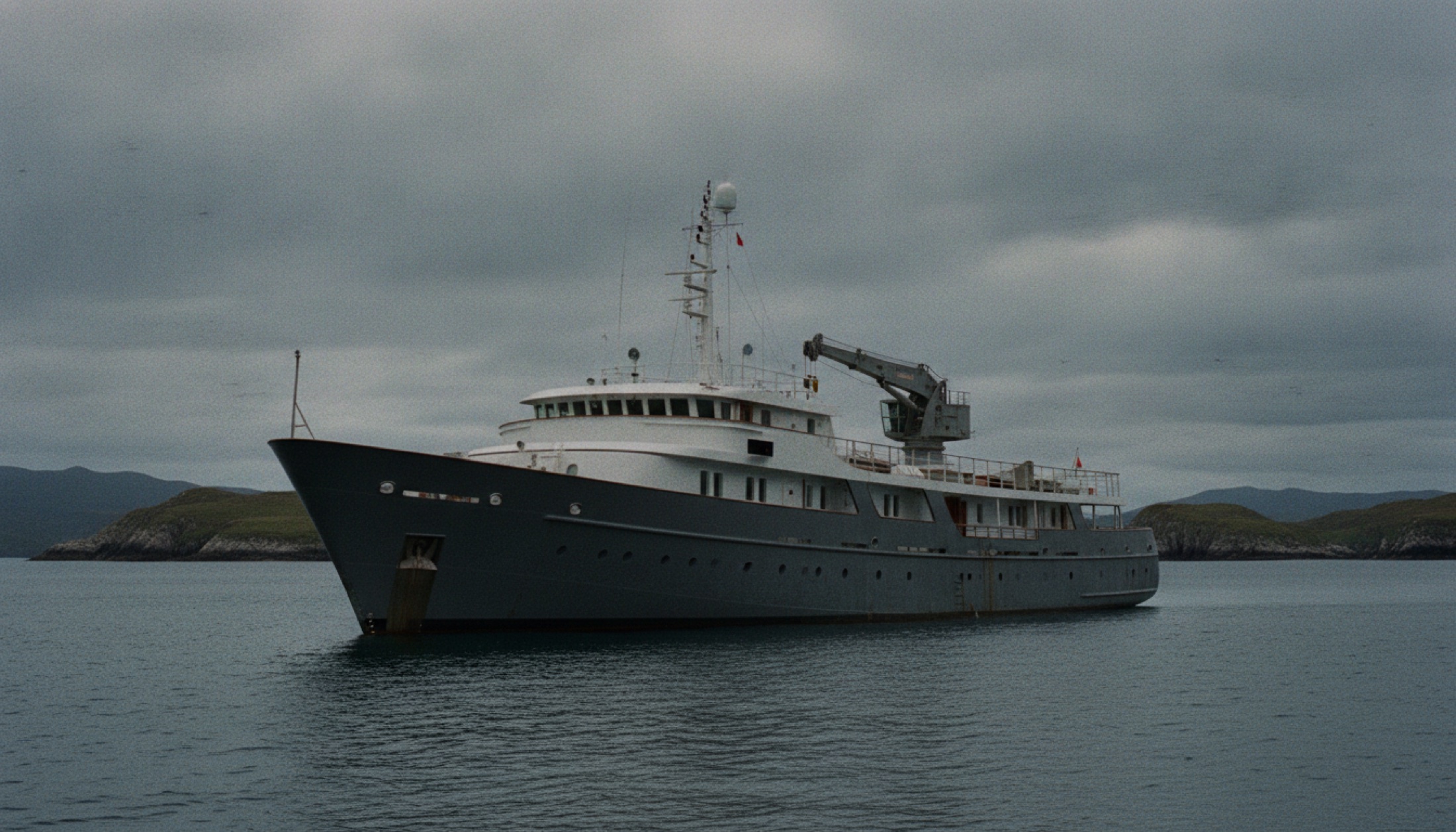 Oceanco Draak, İskoçya kıyılarında demirlemiş haliyle — kıç güvertesinde vinç görünür, çalışan tekne atmosferi