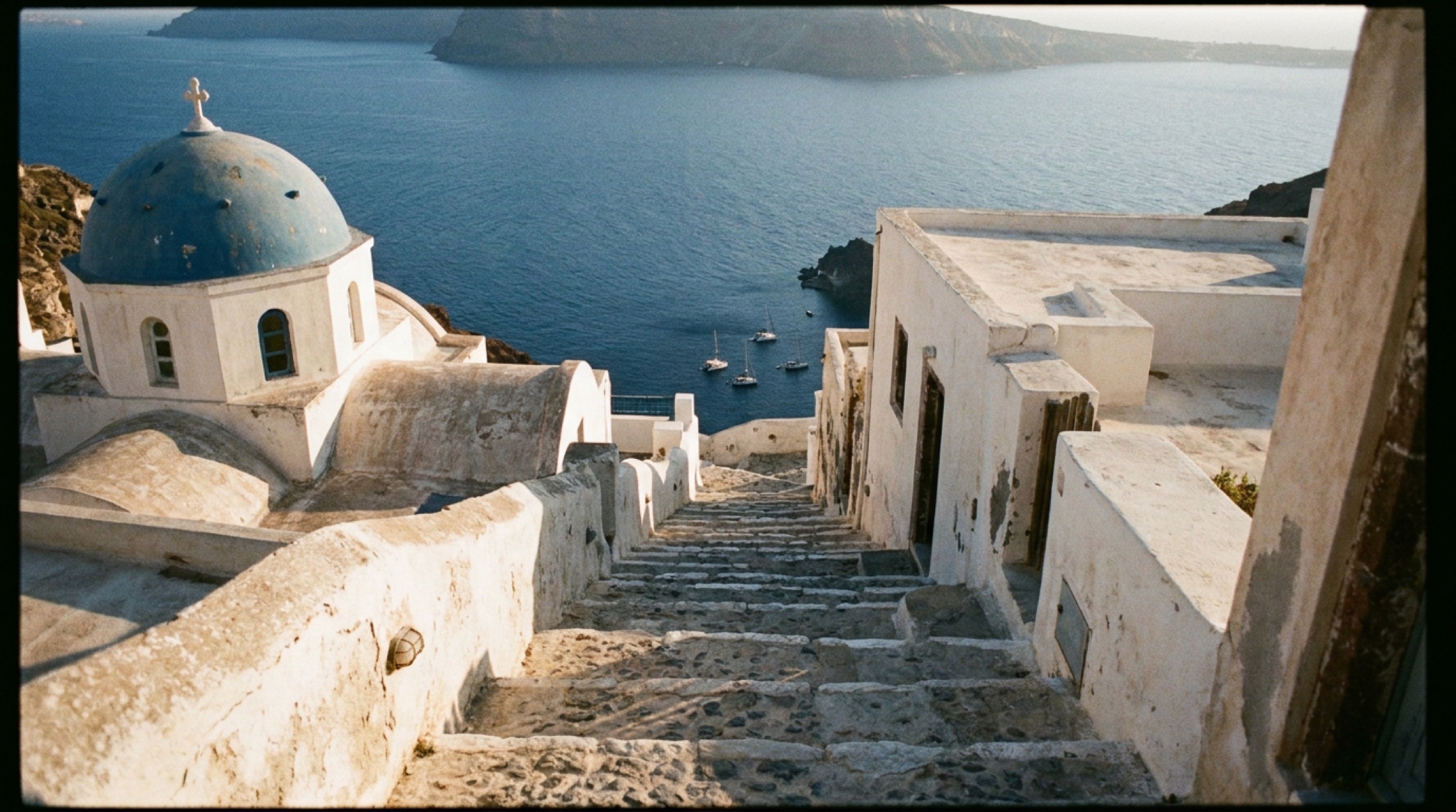 Santorini kaldırım merdivenleri ve alçak güneşte kaldera manzarası — Oia'nın taş dokusu ve mavi kubbe