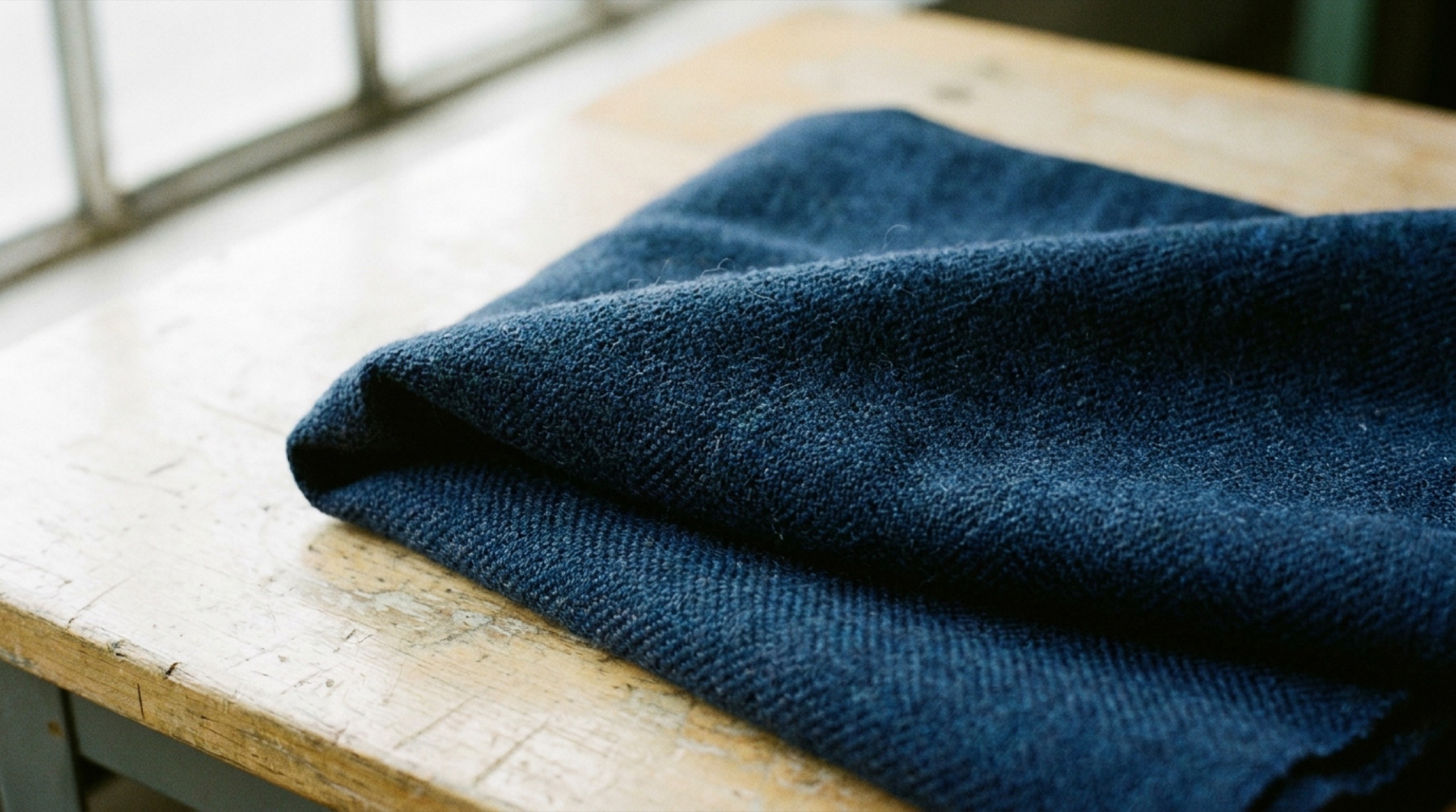 Makro çekimde Merino yününden dokunmuş koyu indigo kumaş yüzeyi, denim dokusunu andıran örgü yapısı görünür.