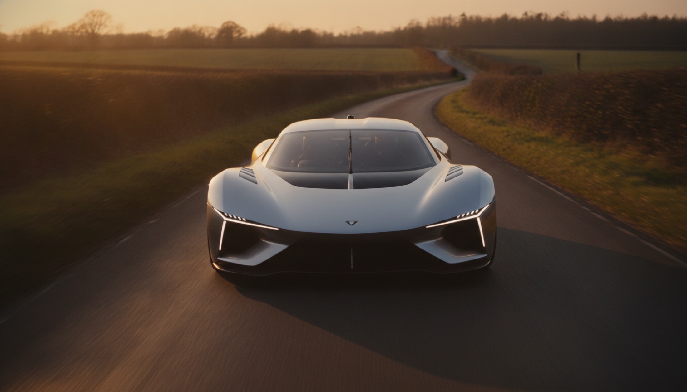 Düşük açıdan çekilmiş aerodinamik hypercar, altın saat ışığında İngiliz kırsalındaki kıvrımlı yolda